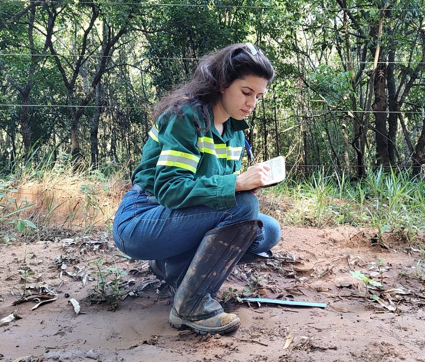 Young conservationist kneeling on mud whilst writing notes in notebook